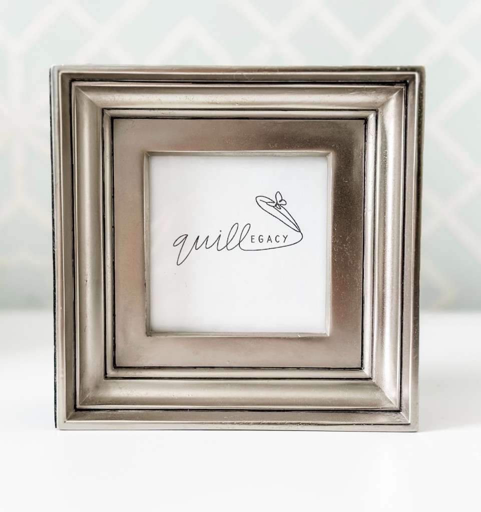 A framed Quillegacy logo card on a shelf against a light blue patterned wall.